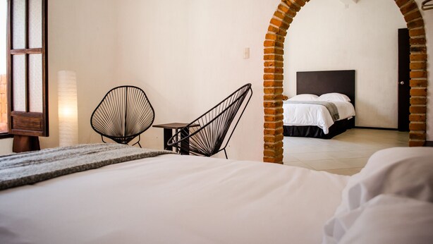 A hotel room with a bed, two chairs, a table, and an arched doorway leading to another room. - Estacion Alameda (Orizaba)