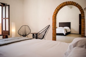 A hotel room with a bed, two chairs, a table, and an arched doorway leading to another room. - Estacion Alameda (Orizaba)