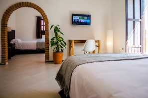 Ein Hotelzimmer mit Bett, Wandfernseher, Topfpflanze, Sessel und einer Bogenöffnung.