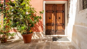 A wooden door with a metal handle, a potted plant, and a tiled floor. - Garden Apartment (Venice)