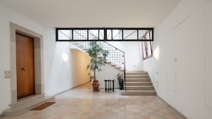 A spacious hallway with a wooden door, a potted plant, a small table, and a staircase with a metal railing. - Garden Apartment (Venice)