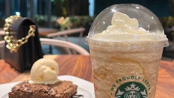 Um copo da Starbucks com chantilly e um brownie com gotas de chocolate e calda de chocolate sobre um prato branco.