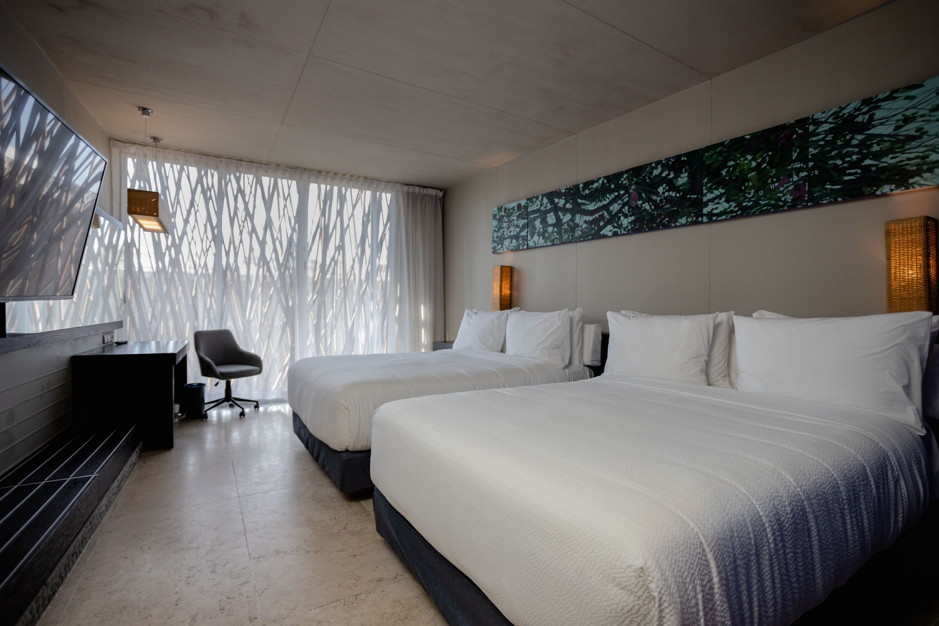 A modern hotel room with two beds, a desk, and a chair.