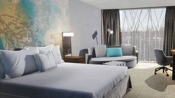 A modern hotel room with a large bed, a desk, a chair, and a view of the city through large windows.