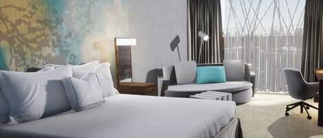 Habitación de hotel moderna con una cama grande, un escritorio, una silla y vistas de la ciudad a través de amplios ventanales.