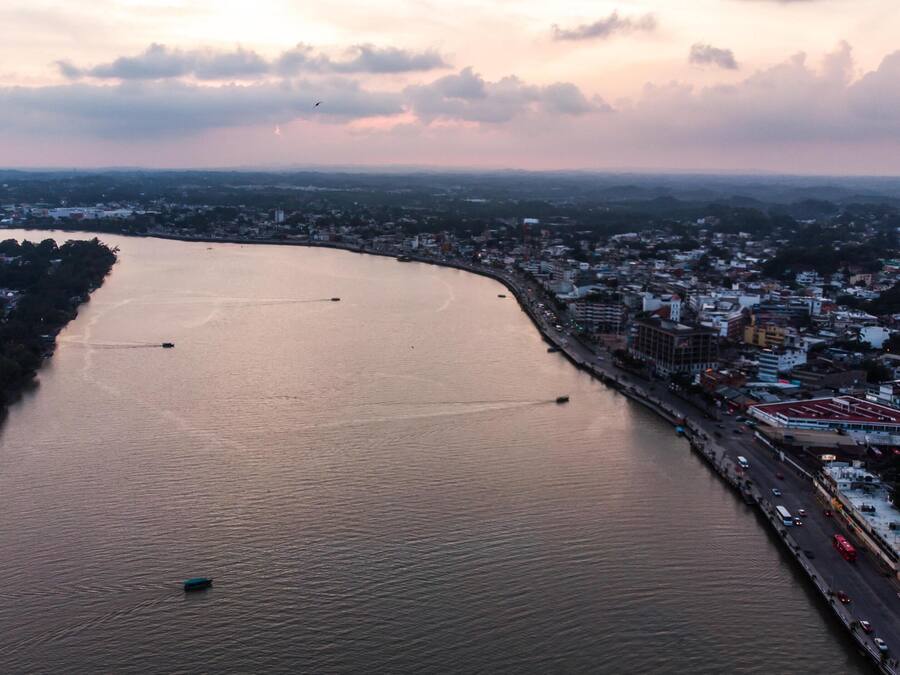 An aerial view of a river with boats, a bridge, and a cityscape with buildings and roads.