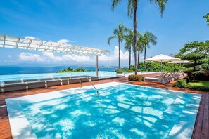 En swimmingpool med utsikt över havet, omgiven av palmer och en pergola.