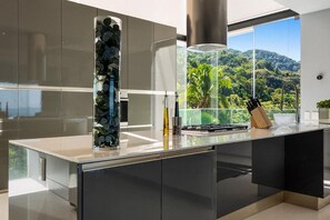 A modern kitchen with a large window overlooking a lush landscape. - Avalon - 901 | 3BR Condo Ocean View & Private Pool (Puerto Vallarta)