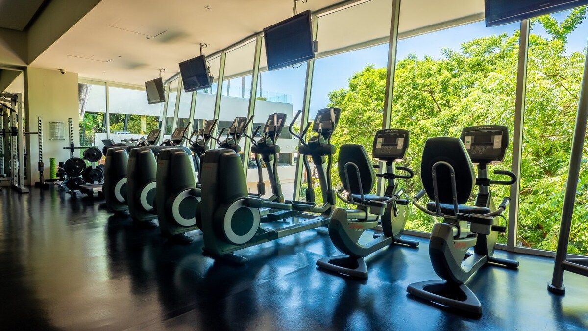 Una palestra con attrezzature cardio e macchinari per pesi, ampie finestre e vista sul verde.