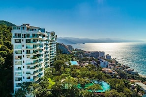A coastal hotel with multiple balconies, a pool, and a view of the sea.