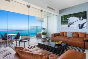 A modern living room with a leather sofa, a glass coffee table, and a view of the sea.