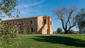 Un edificio de piedra con techo de tejas, una escalera y un gran árbol de fondo.