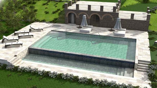 Una piscina con solárium de piedra, sillas de descanso y un edificio con ventanas arqueadas al fondo.