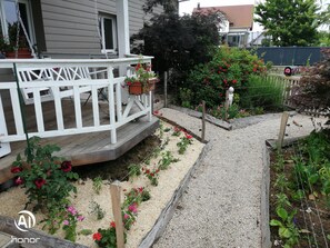 Un jardín con terraza de madera, senderos de grava y diversas plantas florecientes.