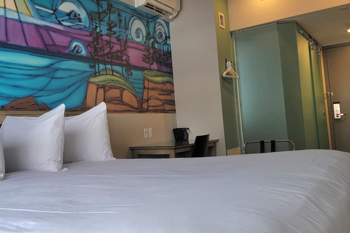 A hotel room with a large bed, a desk, and a colorful mural on the wall.