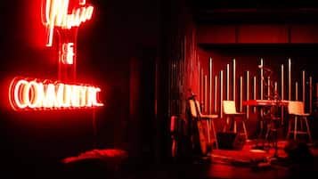 Una habitación tenuemente iluminada con un letrero de neón que dice "MUSIC COMEDY" y un escenario con instrumentos musicales y sillas.