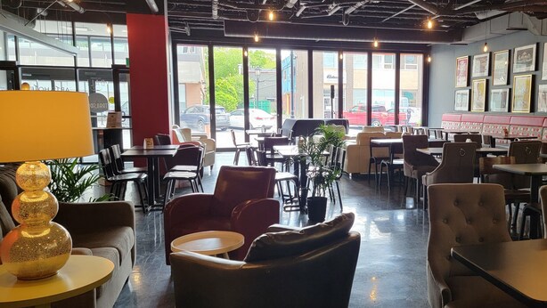 Un restaurante con mesas dentro, ventanas amplias y obras de arte en las paredes.