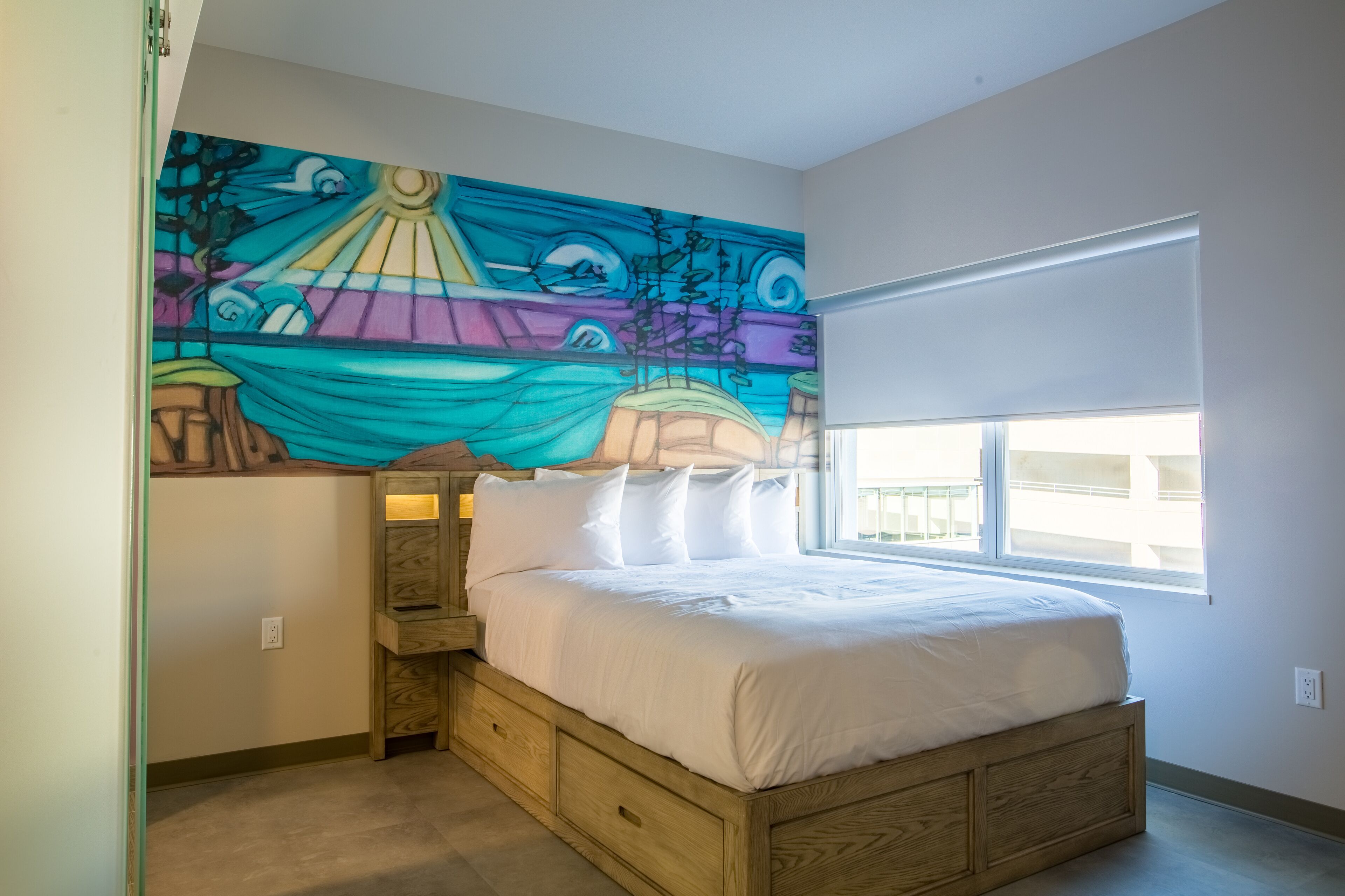 Une chambre à coucher avec un grand lit, une table de chevet, une fresque murale et une fenêtre donnant sur un beau paysage.