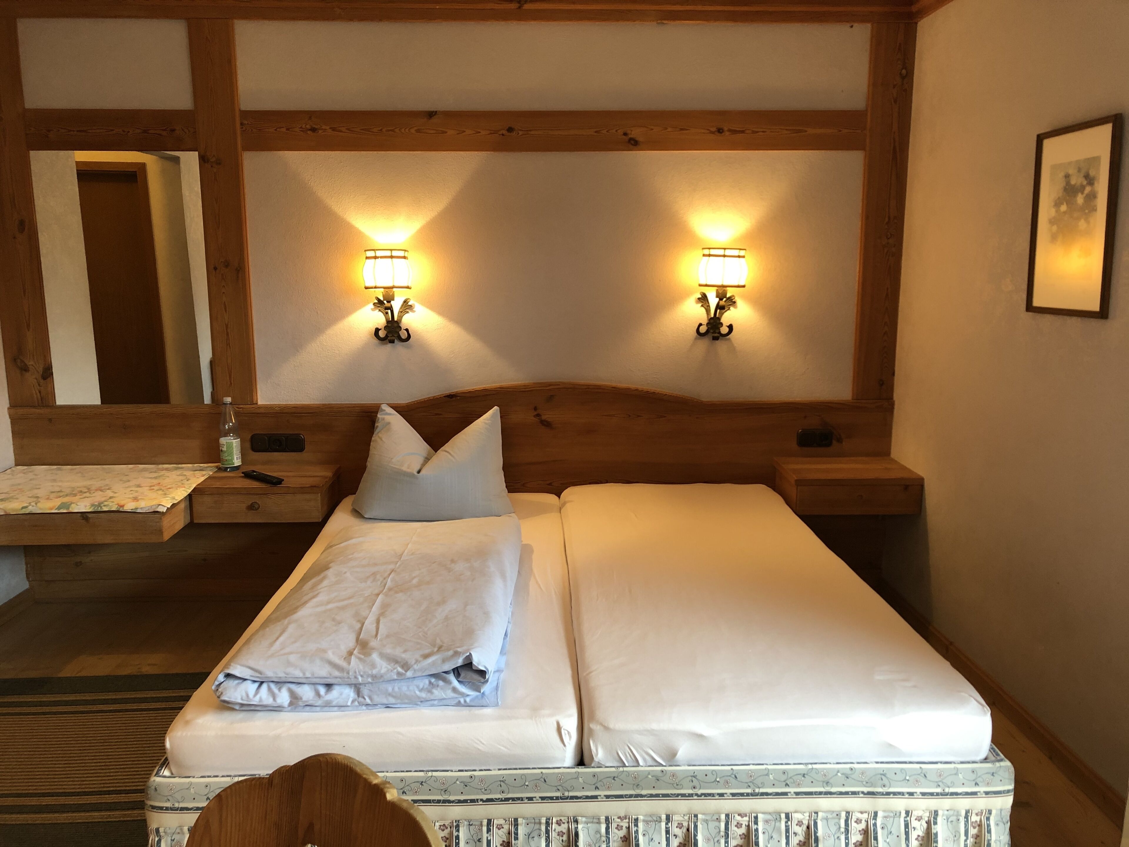 Ein Doppelbett mit zwei Nachttischen, jeder Tisch mit einer Lampe, in einem Zimmer mit Holzbalken an der Decke.