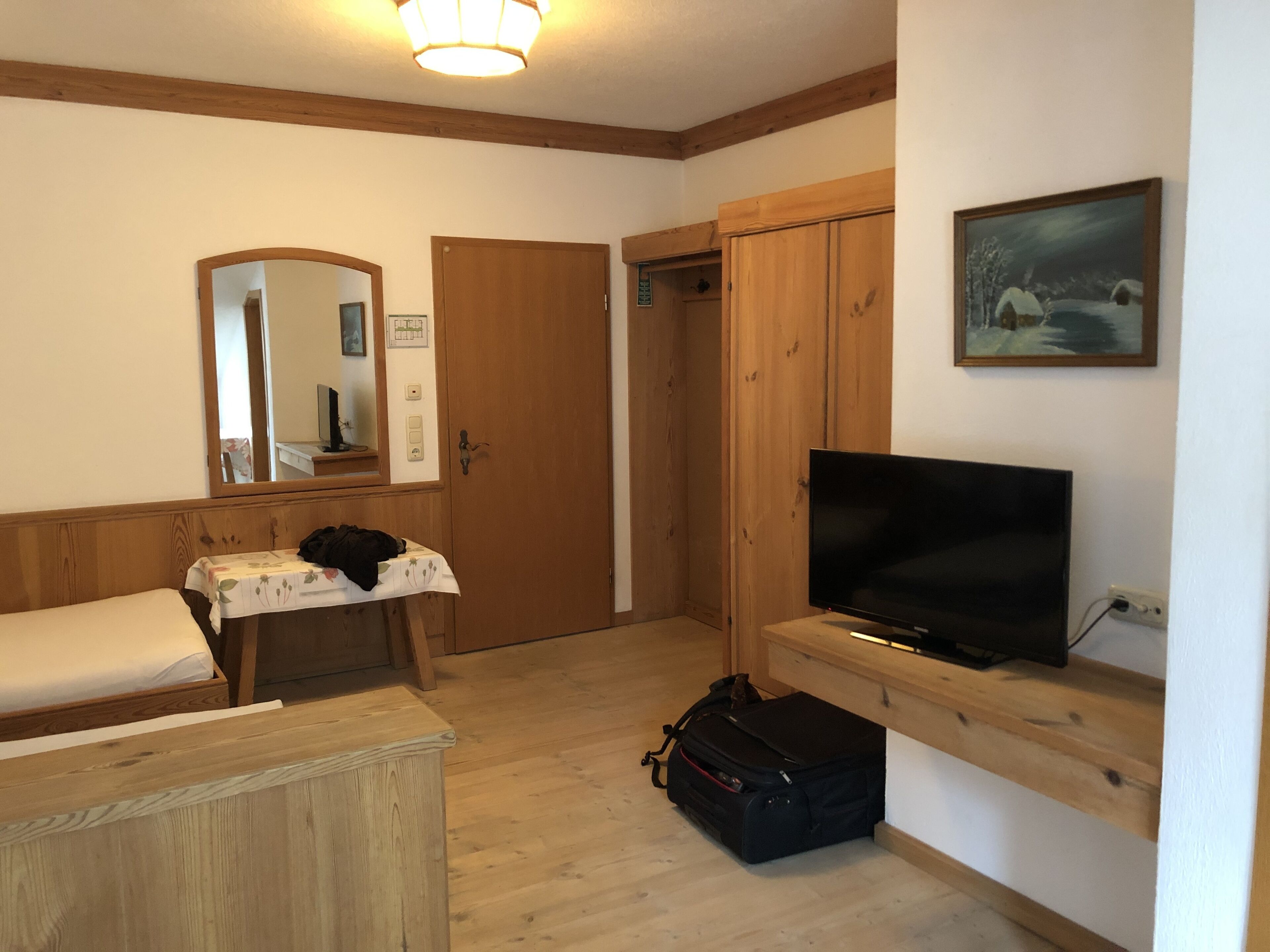 A room with a bed, a desk with a mirror, a television, and a wardrobe.