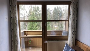 Una habitación con piso de madera, un radiador, una silla y una ventana con vista a árboles.
