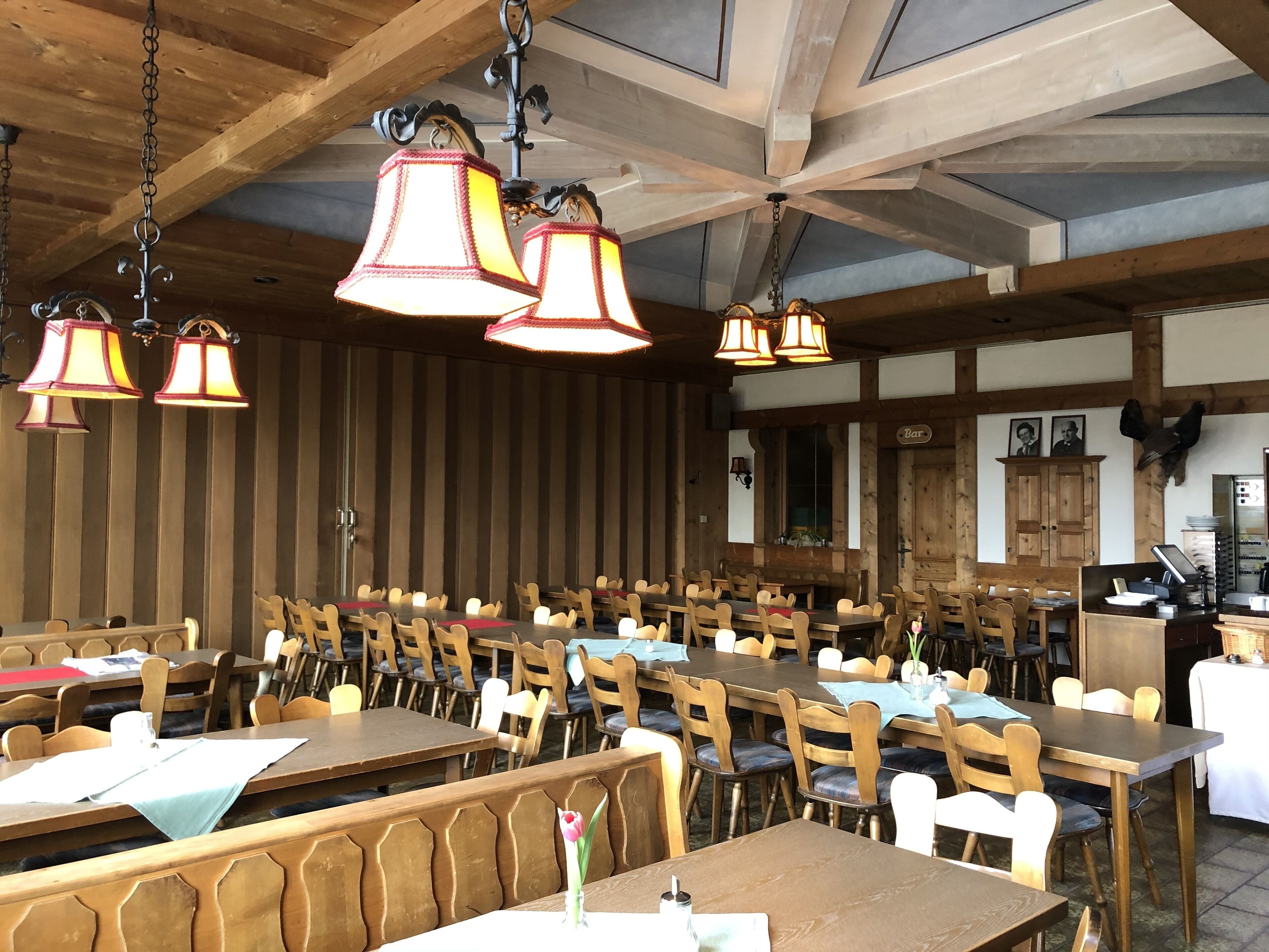 Un restaurante con mesas y bancos de madera, lámparas colgantes y una zona de bar.
