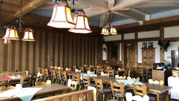 Un restaurante con mesas y bancos de madera, lámparas colgantes y una zona de bar.