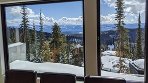 Quarto com grandes janelas que oferecem vista para árvores e montanhas cobertas de neve.
