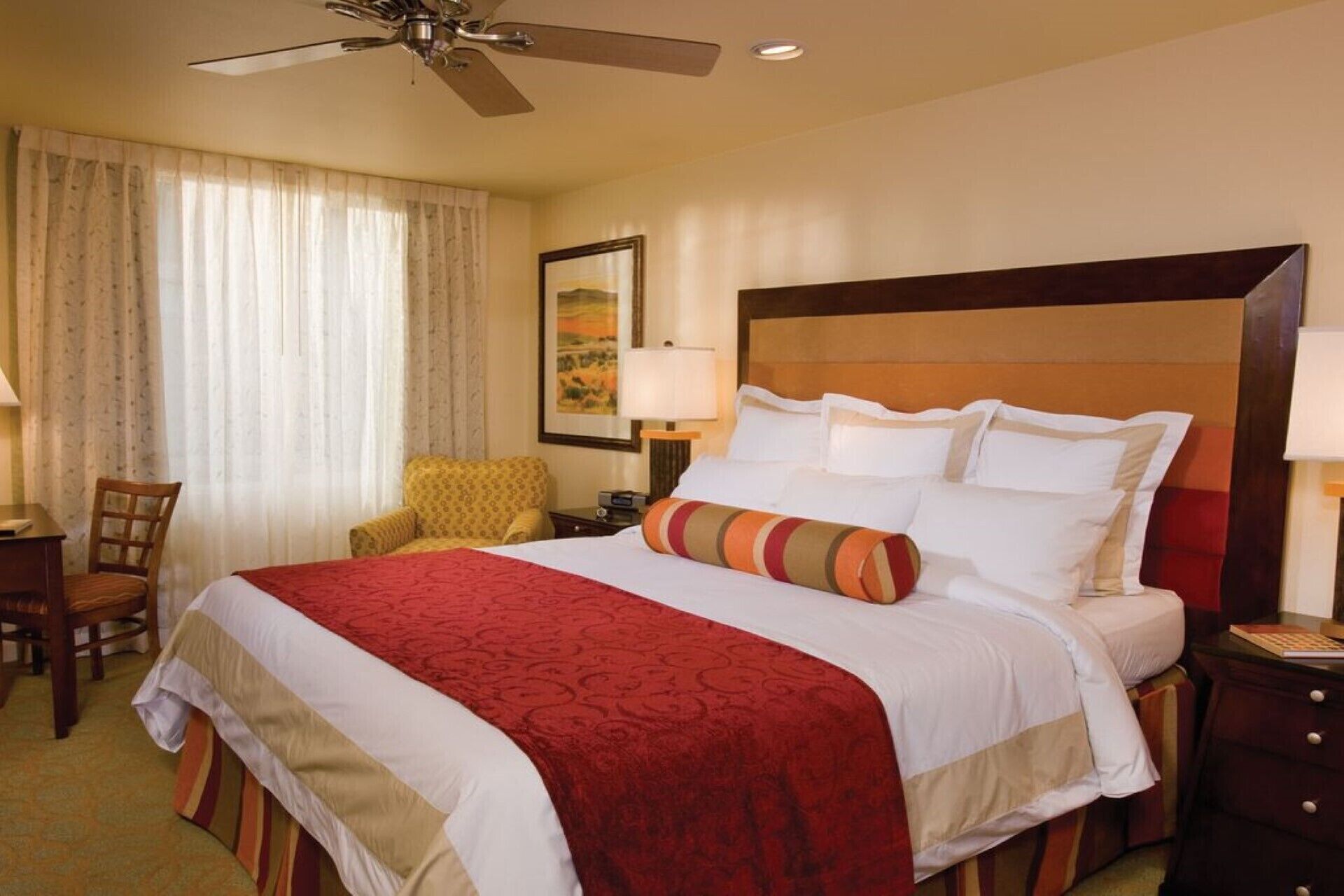 A hotel room with a large bed, a ceiling fan, a chair, and a nightstand with a lamp.