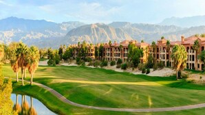 A golf course with a water feature, palm trees, and a building with multiple balconies. - COACHELLA FEST ... 9th- 13th April 2020 (Palm Desert)