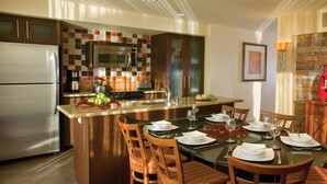 A modern kitchen with a central island, stainless steel appliances, and a dining area with wooden chairs and a glass table. - COACHELLA FEST ... 9th- 13th April 2020 (Palm Desert)