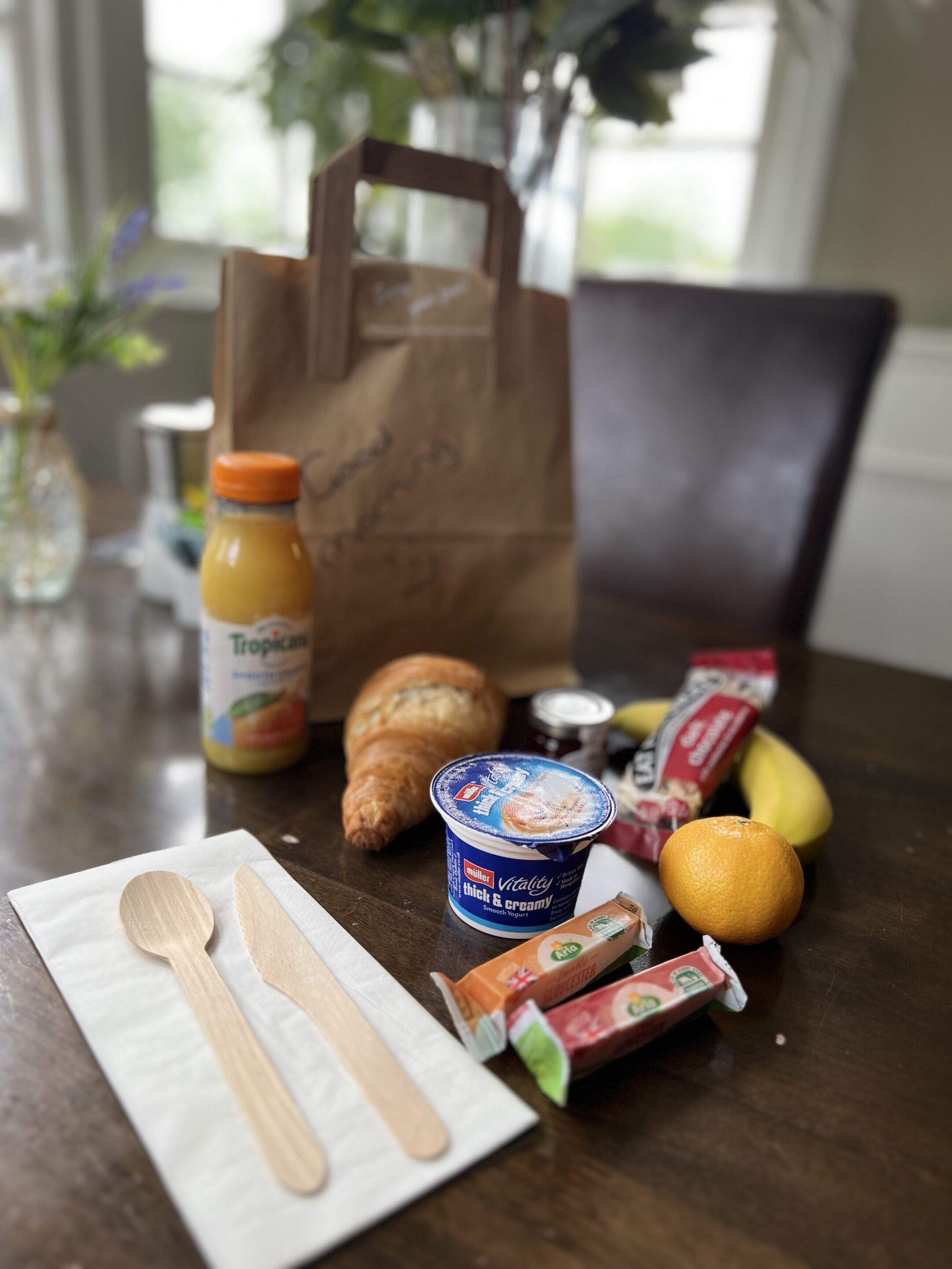 Una mesa con un croissant, yogur, naranja y refrigerios envasados.