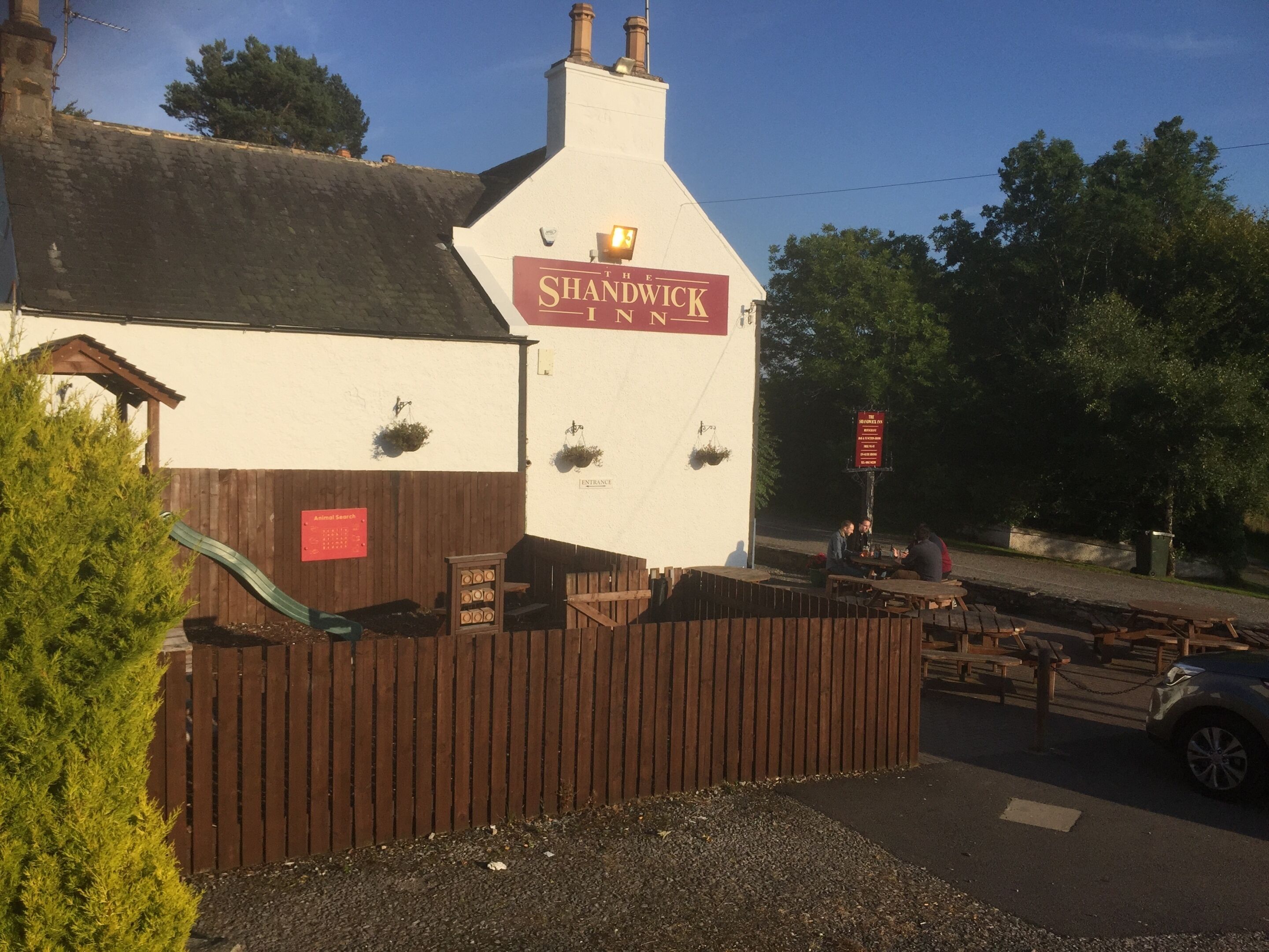 En byggnad med en skylt som visar texten ”The Shandwick Inn” och ett trästaket framför.