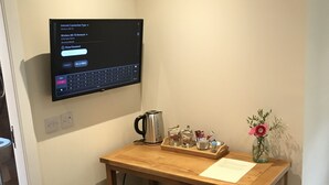 A small wooden desk with a laptop displaying an internet connection type, a kettle, a mug, a cup, and a vase with flowers. - The Shandwick Inn (Invergordon)
