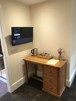 A small wooden desk with a laptop displaying an internet connection type, a kettle, a mug, a cup, and a vase with flowers.