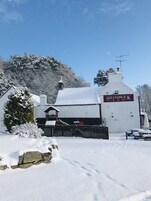 A snow-covered building labeled "SHANDWICK INN" with a stone wall entrance, a wooden fence, and a bench.