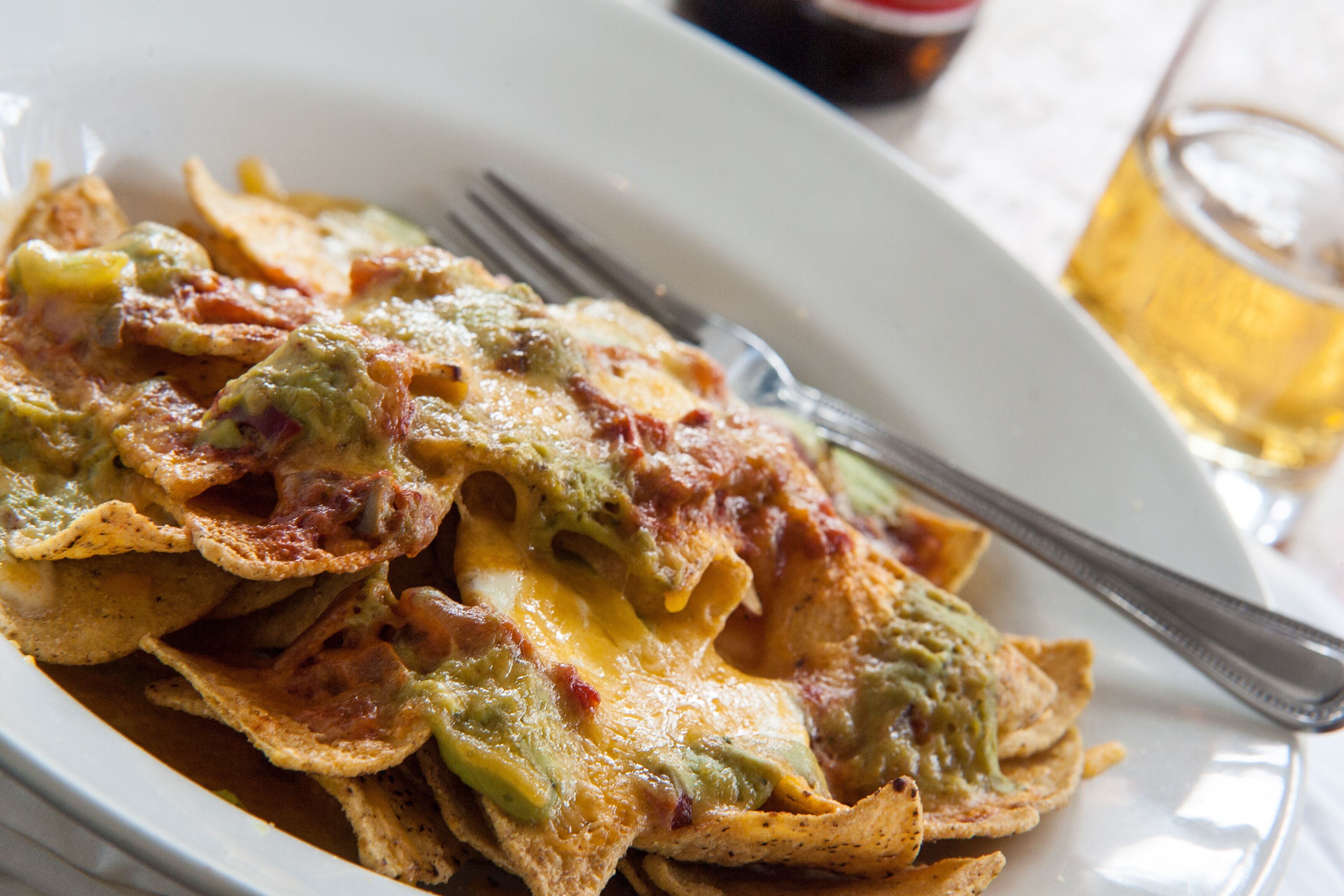 A plate of nachos with melted cheese and green toppings.