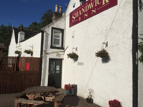 A building with a sign reading "The Shandwick Inn" and a wooden table outside.
