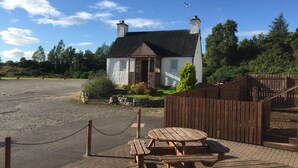 A rustic house with a stone foundation, a wooden fence, and a picnic table area. - The Shandwick Inn (Invergordon)