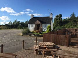 A rustic house with a stone foundation, a wooden fence, and a picnic table area.
