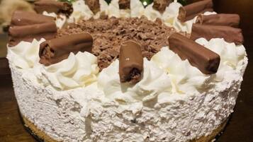 A round cake with whipped cream and chocolate pieces on top, placed on a wooden table.