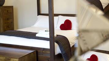 Ein Himmelbett mit weißen Leinentüchern und herzförmigen roten Kissen.