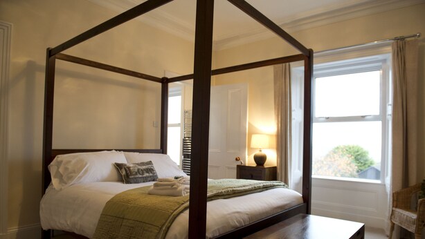 Uma cama com dossel de madeira, uma mesa de cabeceira e um abajur.