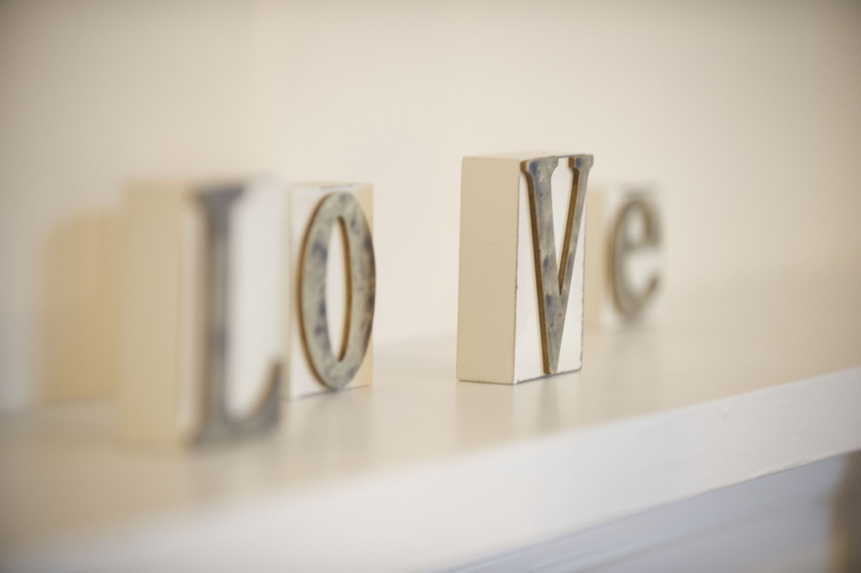 Une étagère blanche ornée de lettres métalliques formant le mot « AMOUR », le tout dans un style minimaliste.