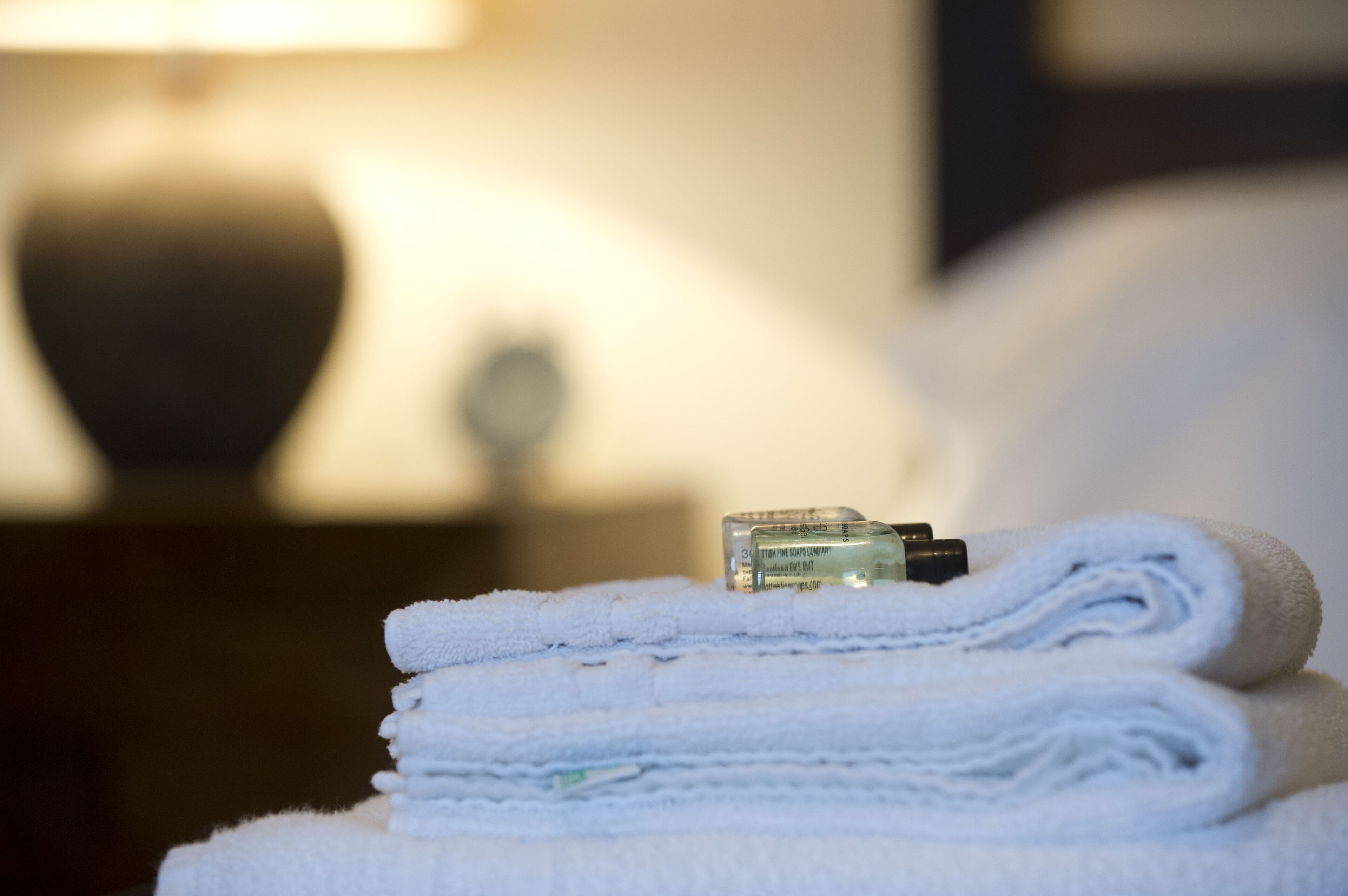 A stack of white towels with a bottle of lotion on top.