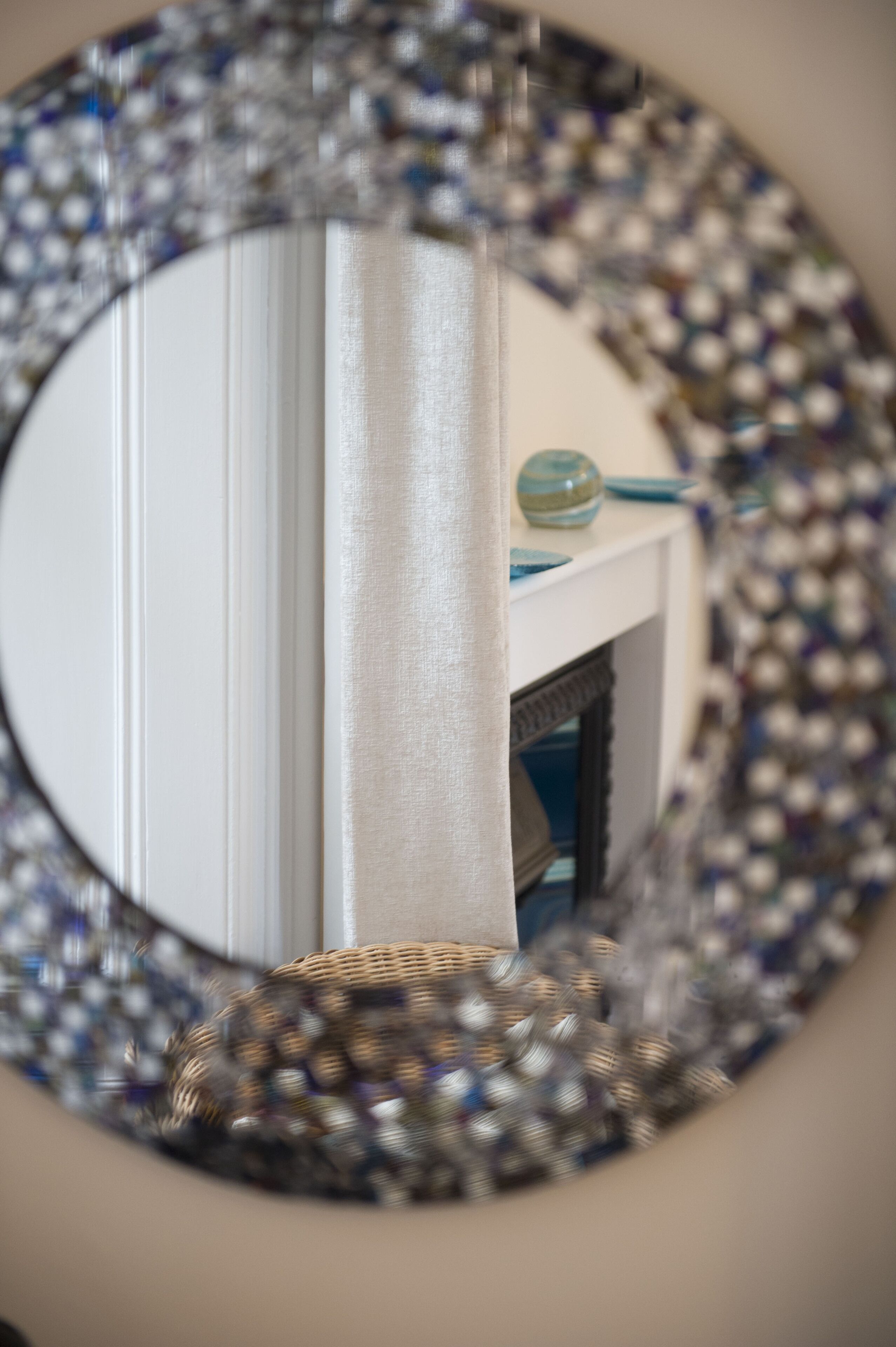 Een spiegel met een decoratief lijstwerk, reflecteert een witte muur en een open haard met een blauwe vaas.