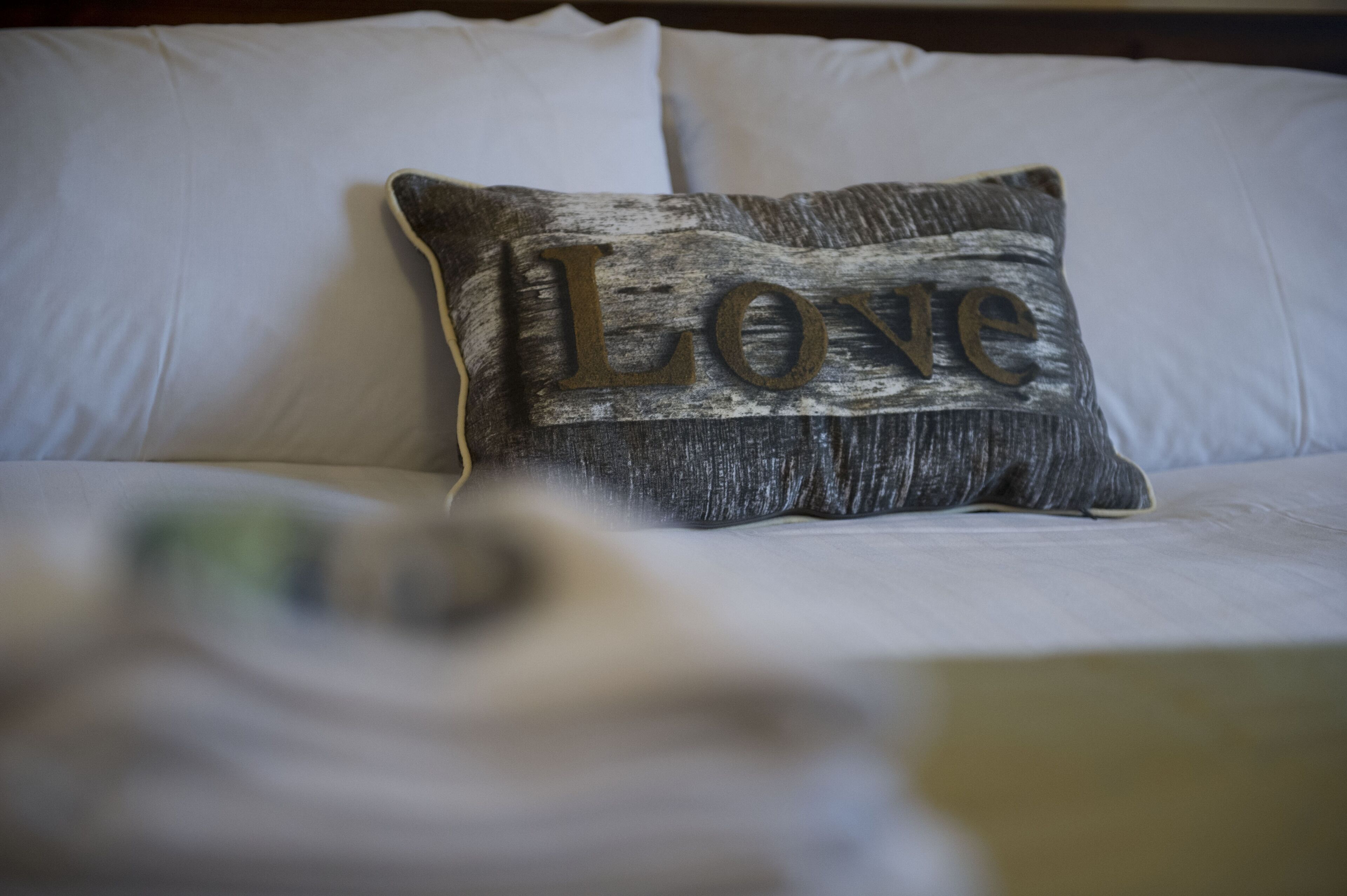 A bed with white linens and a pillow with the word "Love" on it.