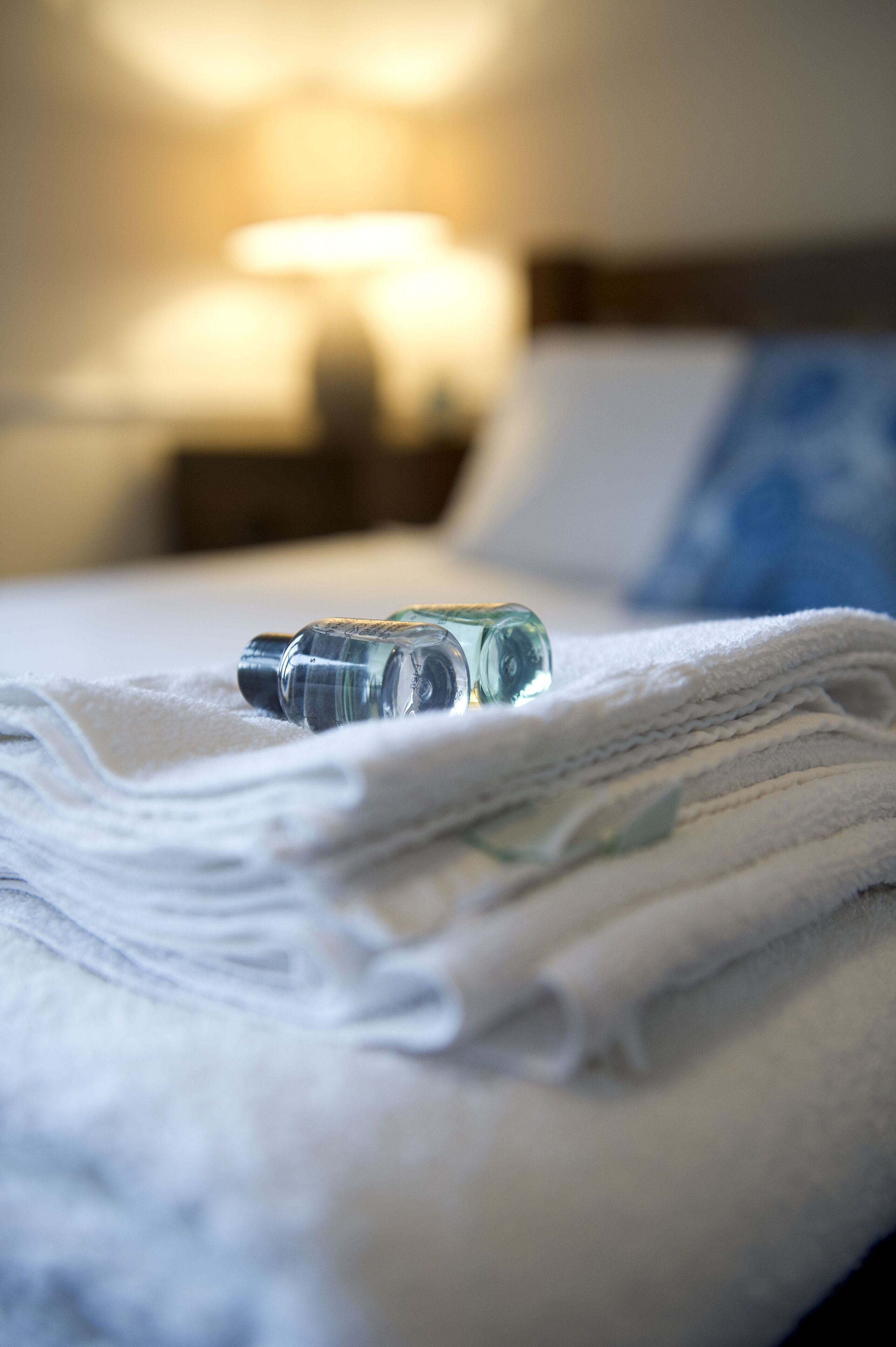 Una cama con una toalla blanca doblada y una botella de vidrio transparente encima.