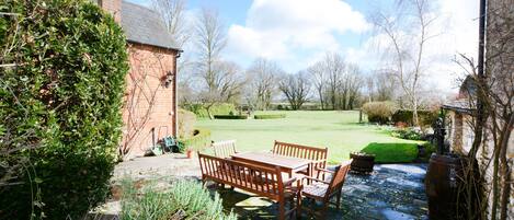 A brick building with a stone patio, wooden furniture, and a lawn.