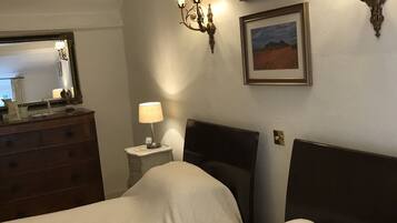 Camera d'albergo con due letti, una cassettiera, un comodino con lampada e applique a parete.